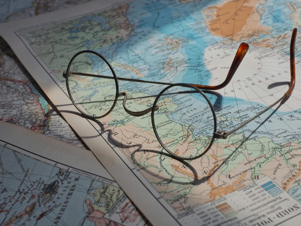 Passport , Visa Agency & Other Documentation (Non-Government) Round vintage eyeglasses resting on a vibrant historical world map, capturing a sense of exploration.