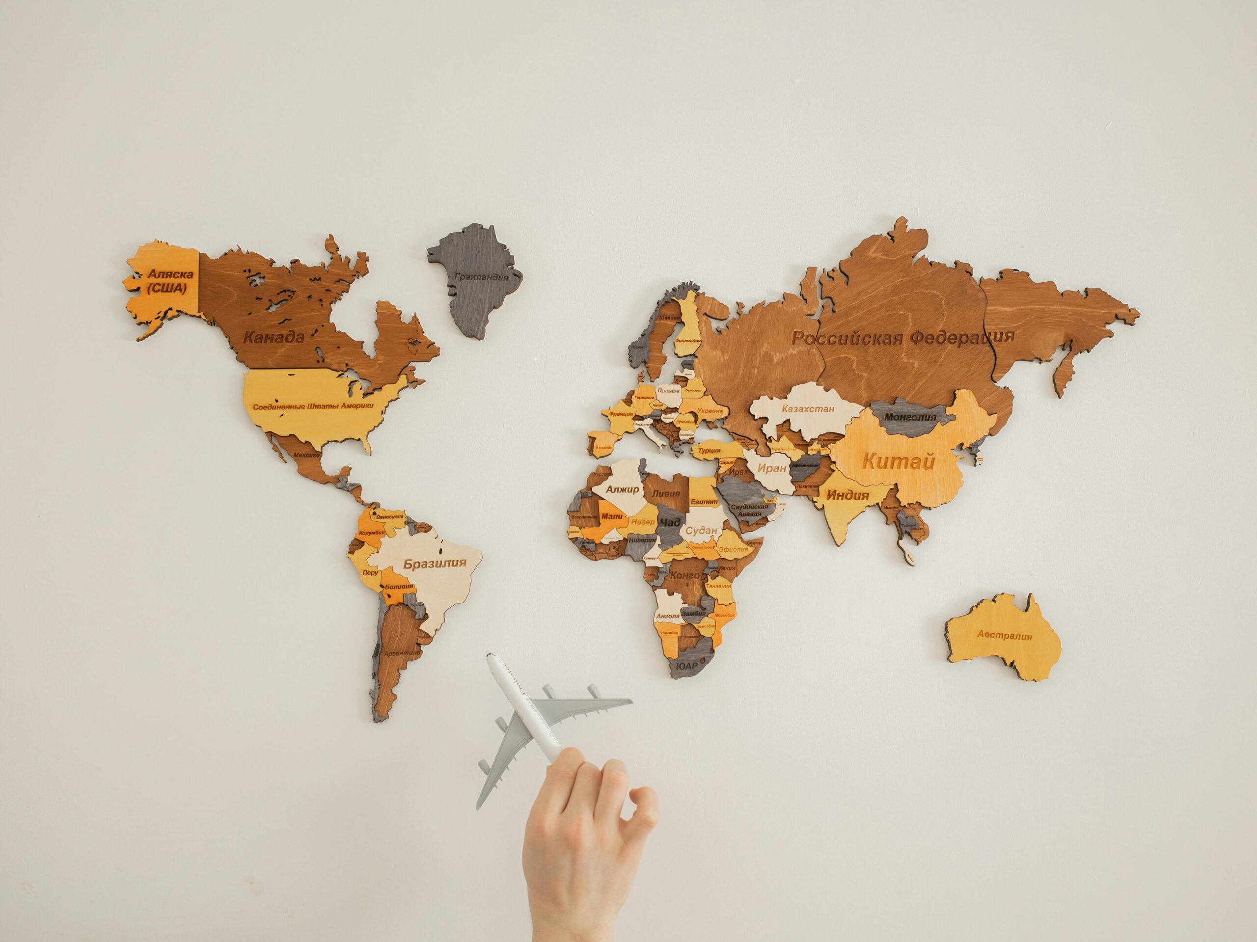 Passport , Visa Agency & Other Documentation (Non-Government) Crop unrecognizable person with toy aircraft near multicolored decorative world map with continents attached on white background in light studio